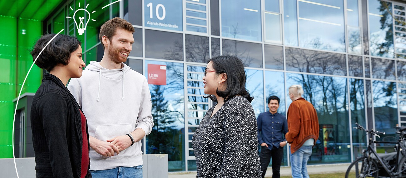 Menschen unterhalten sich in kleinen Gruppen vor einem Gebäude mit Glasfront.